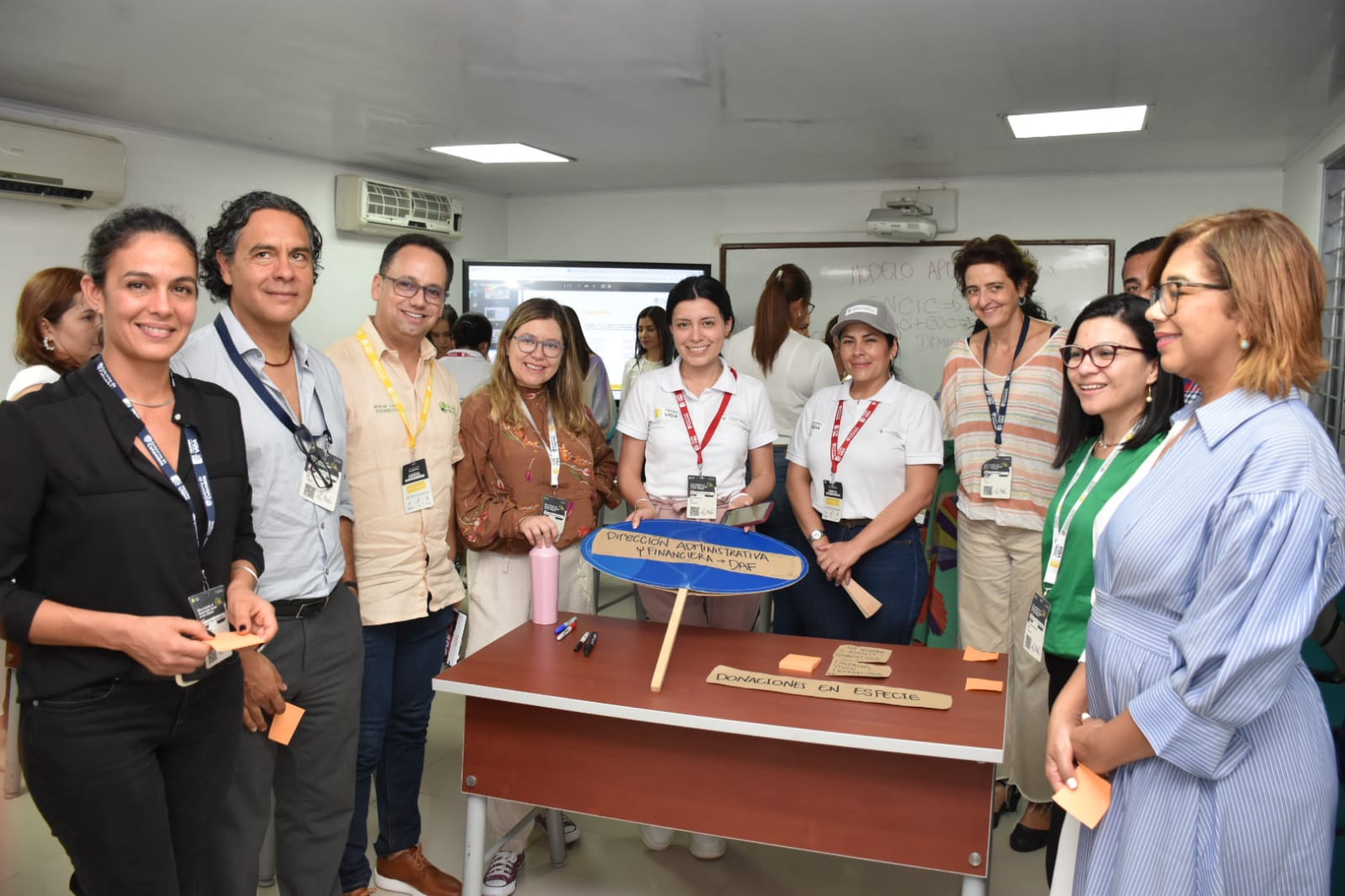 En la foto se encuentran10 personas, 2 facilitadoras del Modelo APC Colombia con camiseta blanca, en sus manos sostienen un cartel de la dirección “Administrativa y financiera” que representaban para el Modelo. Este Modelo se realizó en la Universidad Popular del Cesar en el marco de la conmemoración de la Cooperación Sur-Sur 2023