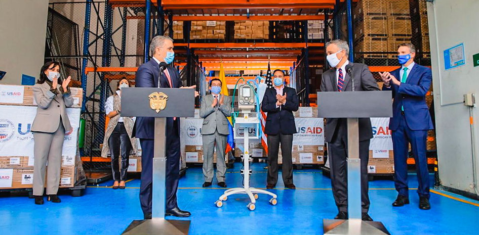 Imagen del Presidente Duque y el embajador de Estados Unidos con sus equipos de trabajo, en la bodega donde estan las cajas con la donación de USAID