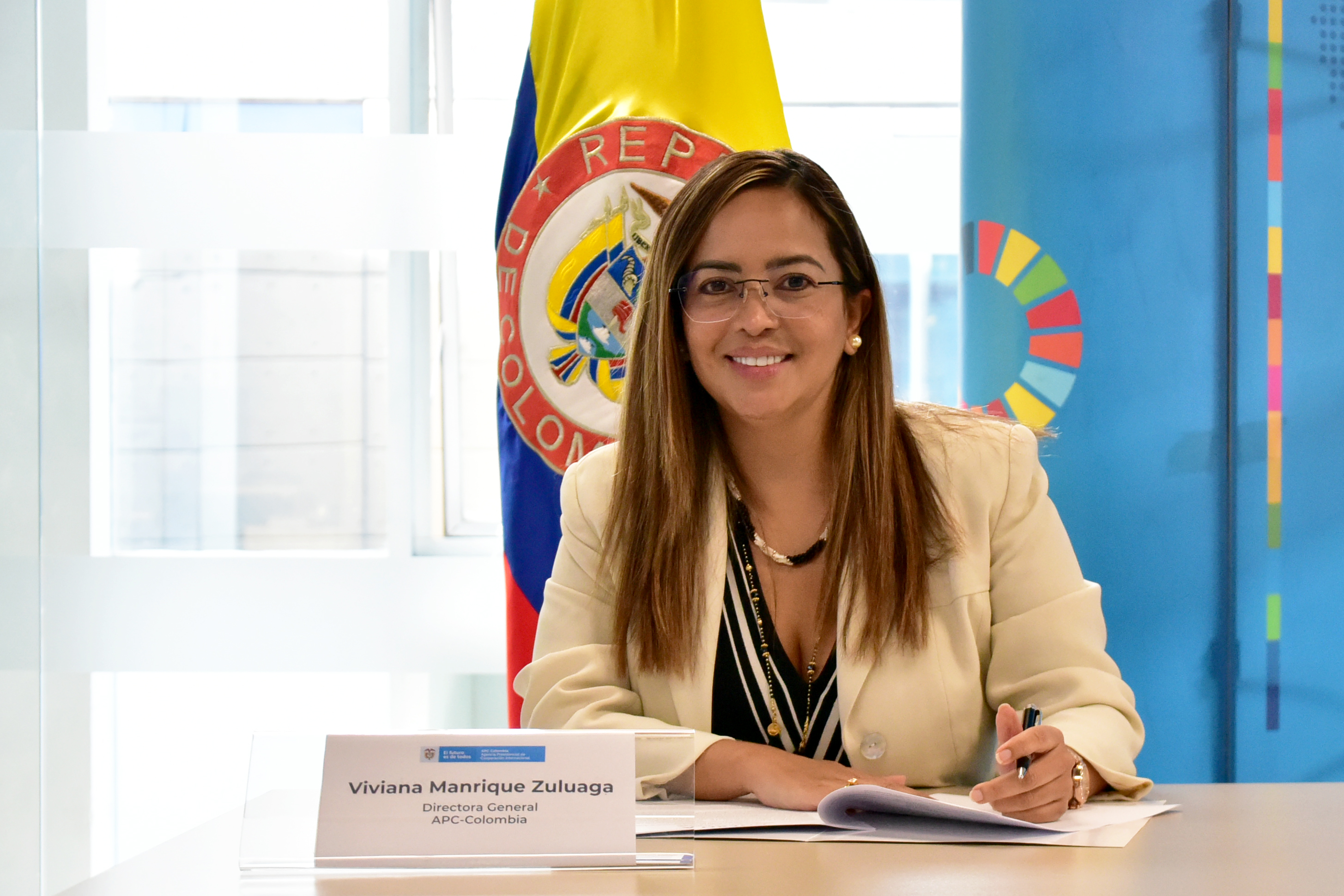 Foto de la directora Viviana Manrique con una chaqueta color beige y con la bandera de Colombia en la parte de atrás.