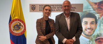 En el medio la directora general de APC-Colombia, Eleonora Betancur González, a la derecha el embajador de Argentina en Colombia, Gustavo Dzuluaga, a la izquierda, la bandera de Colombia