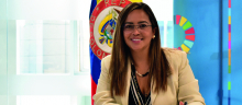 La directora de APC-Colombia, Viviana Manrique Zuluaga Firmando el documento, detrás de ella la bandera de Colombia